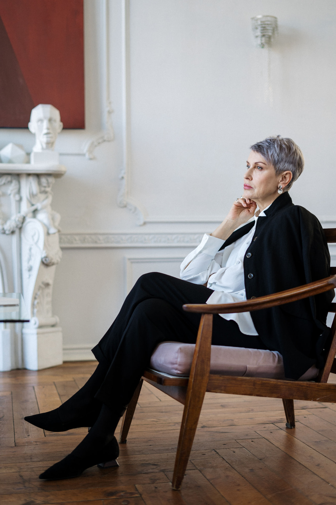 Woman seated beside a white wall in an elegant interior