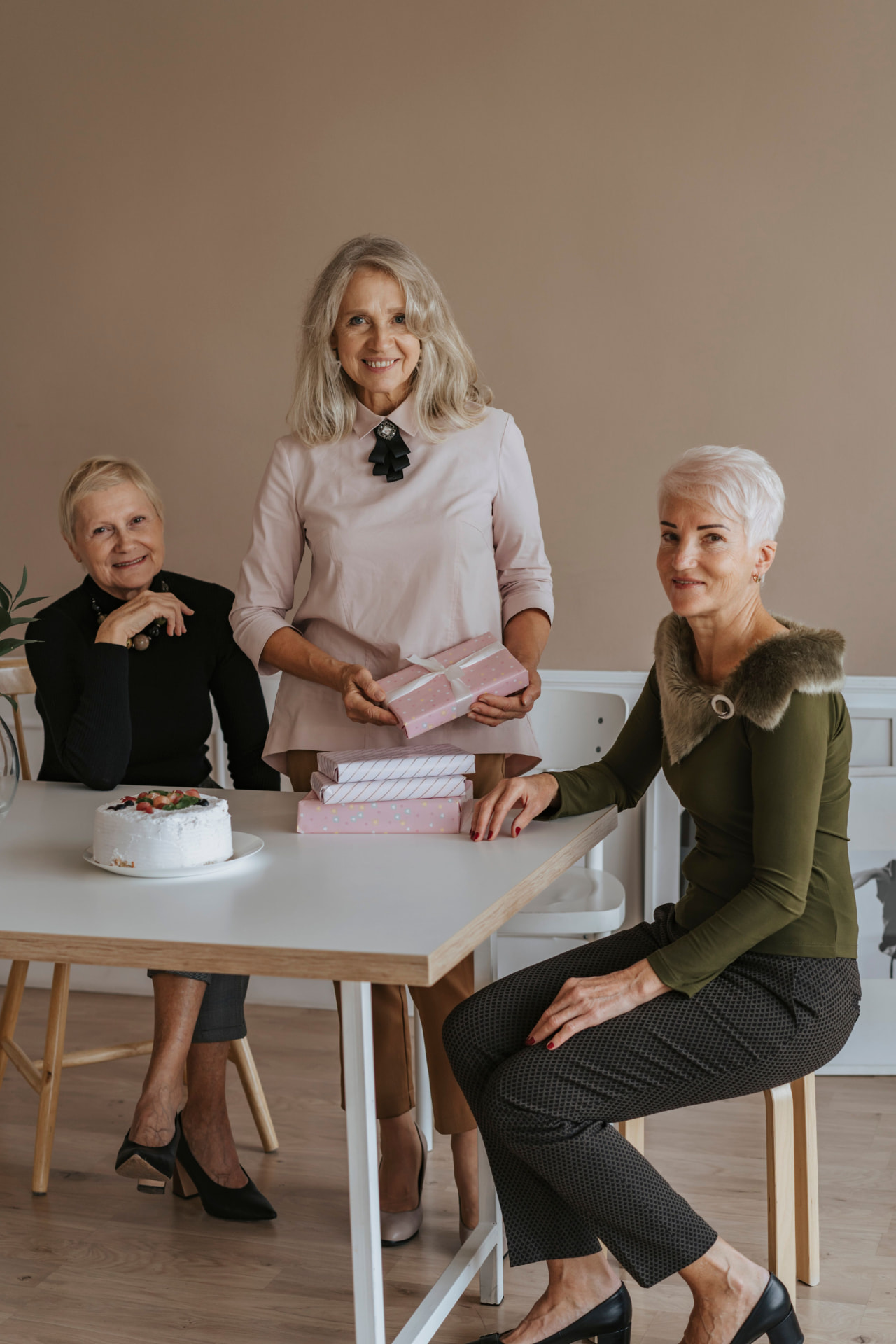 Three women gathered around a table with gifts and a cake
